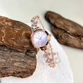 elógio feminino sofisticado, com caixa redonda em liga metálica, mostrador clássico com números árabes e ponteiros em formato de folha. Pulseira delicada com detalhes em strass, combinando charme e estilo