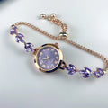 elógio feminino sofisticado, com caixa redonda em liga metálica, mostrador clássico com números árabes e ponteiros em formato de folha. Pulseira delicada com detalhes em strass, combinando charme e estilo