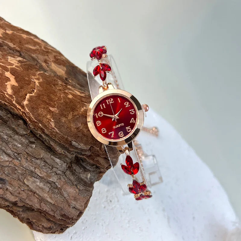 elógio feminino sofisticado, com caixa redonda em liga metálica, mostrador clássico com números árabes e ponteiros em formato de folha. Pulseira delicada com detalhes em strass, combinando charme e estilo